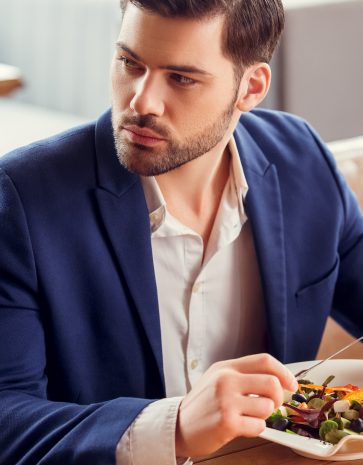 youngmansittingattableinrestauranteatingvegetablesalad